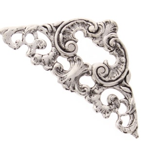 May include: Silver corner bracket with a decorative, ornate design. The bracket is made of metal and has a filigree pattern.