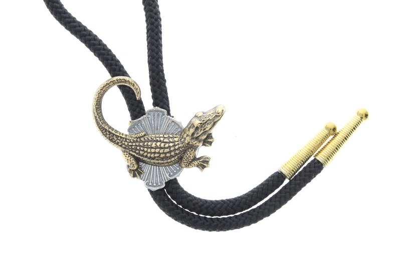 May include: A black bolo tie with gold-toned tips and a decorative alligator pendant. The alligator is detailed with scales and has a curled tail.