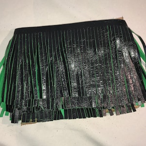 May include: Black and green fringe trim with a shiny, textured finish. The fringe is approximately 1 inch wide.