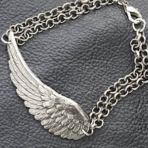 May include: A silver chain bracelet with a detailed silver wing pendant. The wing is textured and has a realistic design.