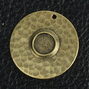 May include: A round, hammered brass pendant with a smaller, round, recessed area in the center. The pendant has a hole at the top for hanging.