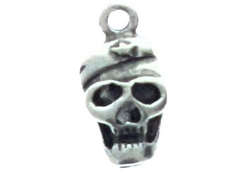 May include: Silver charm of a skull with a bandage on its head. The skull has a detailed face with eye sockets, a nose, and a mouth.