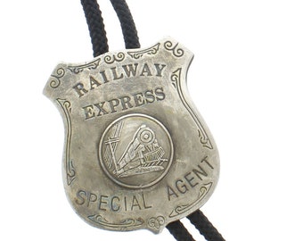 May include: A silver bolo tie with a Railway Express Special Agent badge. The badge features a train engine and the words "Railway Express" and "Special Agent".