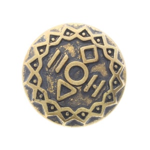 Könnte beinhalten: Ein runder, goldfarbener Metallknopf mit einem schwarzen und goldenen geometrischen Design. Der Knopf zeigt einen Kreis, ein Dreieck, ein Quadrat und Linien.