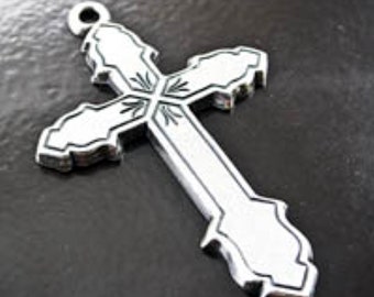 May include: A silver-colored cross pendant with an ornate design. The cross features a detailed pattern at the intersection and along the edges. It has a loop at the top for hanging.