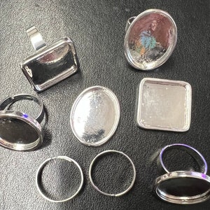 May include: Assortment of silver-toned ring blanks with round and square bezel settings. The ring blanks are ready for crafting and customization.