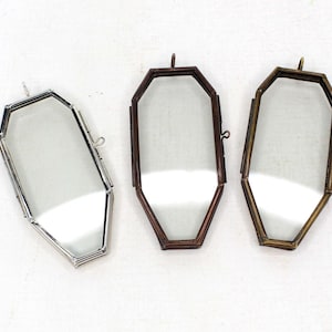 May include: Three octagonal-shaped glass picture frames with metal frames. The frames are silver, brass, and bronze in color. The frames are open on the back and have a small loop at the top for hanging.