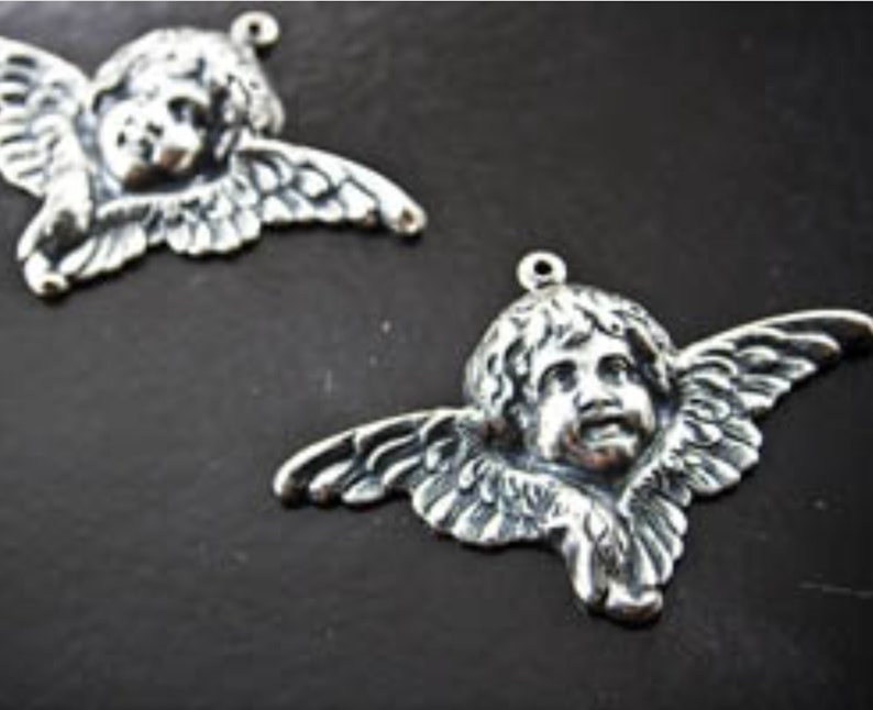 Puede incluir: Dos encantos de querub&iacute;n de plata con alas y una cara detallada. Los encantos tienen un bucle en la parte superior para sujetarlos a joyas u otras manualidades.