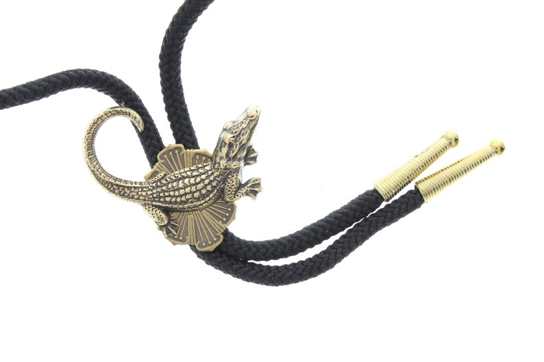 May include: A black bolo tie with gold-colored tips and a decorative alligator pendant.