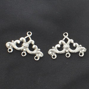 Puede incluir: Dos adornos decorativos de metal plateados con un diseño de espiral adornado. Cada adorno tiene tres bucles para sujetar a una pieza de joyería más grande.