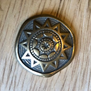 Puede incluir: Un diseño de estrella dorada en metal con una estrella central y círculos concéntricos de elementos decorativos.