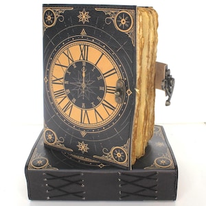 May include: A black journal with a clock face design in gold. The journal is locked with a metal clasp and sits on a matching base. The pages have a textured, aged appearance.