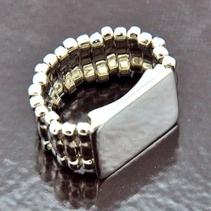 May include: A silver adjustable ring with a rectangular band. The band is made of multiple rows of small, round beads.