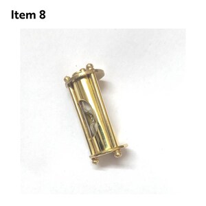 May include: A gold-colored hourglass with a clear glass center. The hourglass is about 2 inches tall and has a cylindrical shape.