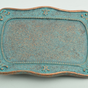 May include: A decorative metal tray with a turquoise blue finish and a copper-colored border. The tray has a scalloped edge and a raised design around the perimeter.