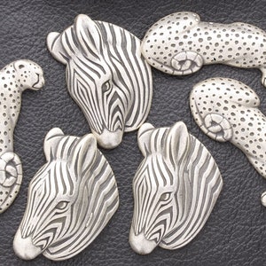 May include: Five silver animal figurines, including two zebras and three leopards. The zebras have black and white stripes, and the leopards have black spots. The figurines are all facing forward and are arranged in a semi-circle.
