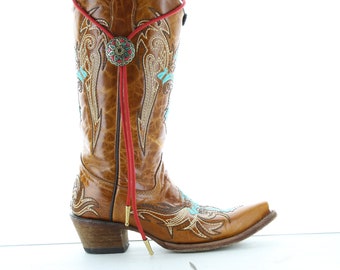 Könnte beinhalten: Brauner Leder-Cowboystickel mit türkisfarbener und goldener Stickerei. Der Stiefel hat eine rote Stiefelschnur mit einem goldenen Metallakzent.