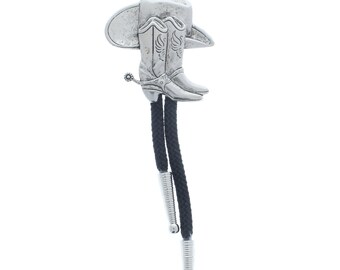 Puede incluir: Un corbatín bolo plateado con un diseño de bota y sombrero de vaquero. La corbata es negra con puntas plateadas.