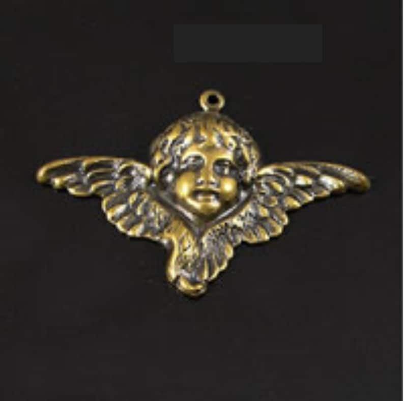 Puede incluir: Un amuleto de metal dorado con un querub&iacute;n con alas. El querub&iacute;n tiene una cara redonda con una expresi&oacute;n dulce y lleva una corona.