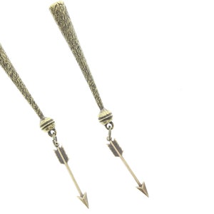 May include: A pair of gold-toned earrings with arrowhead charms hanging from the bottom. The earrings are long and slender, with a textured surface.
