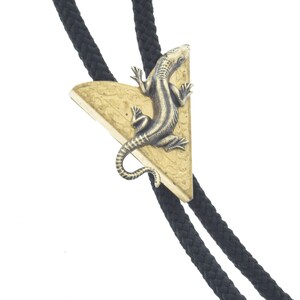 Könnte beinhalten: Ein schwarzer Bolo-Krawattenhalter mit einem dreieckigen Anhänger mit einem goldfarbenen Eidechsen-Design.