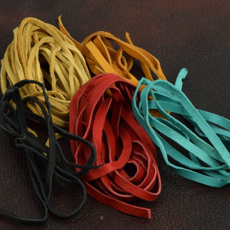 May include: Assortment of leather cords in various colors, including black, red, yellow, and turquoise. The cords are arranged in a loose pile on a brown surface.