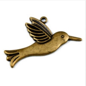 Peut inclure: Un charme en forme de colibri de couleur bronze avec un design d'aile détaillé. Le charme a une boucle en haut pour l'attacher à un collier ou un bracelet.