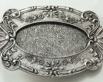 Könnte beinhalten: Ein ovaler Rahmen aus silberfarbenem Metall mit einem verzierten Design. Der Rahmen hat eine strukturierte Oberfläche und einen erhöhten Rand.