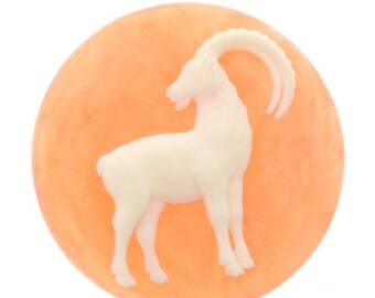 May include: A round, peach-colored soap with a white, raised image of a goat with horns.