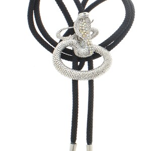 May include: A black bolo tie with a silver snake pendant encrusted with clear rhinestones.