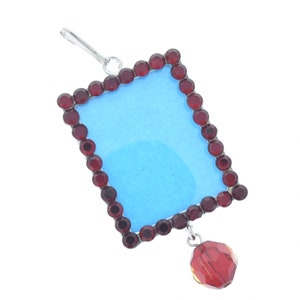 May include: A silver picture frame with a blue background and a red crystal dangle. The frame is decorated with a border of red rhinestones.