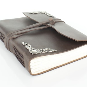 May include: A brown leather-bound journal with a flap closure and silver metal accents. The journal is tied closed with a brown leather strap.