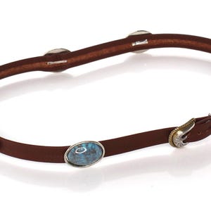 May include: A thin brown leather belt featuring multiple oval-shaped blue and brown marbled stone inlays set in silver-toned metal frames. The belt includes a silver-toned metal buckle with intricate engraved detailing and a matching metal keeper.