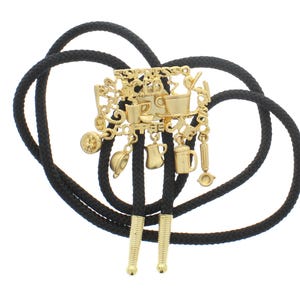 May include: A gold-tone bolo tie featuring a coffee-themed charm with multiple charms, including a coffee pot, a cup of coffee, and a coffee bean. The bolo tie is on a black cord.
