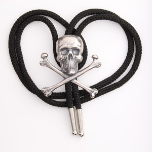 May include: A black bolo tie with a silver skull and crossbones pendant. The tie is in the shape of a heart.