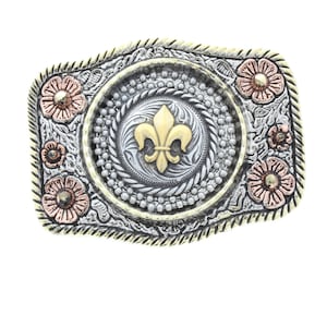 Pode incluir: Uma fivela de cinto prateada com um design de flor-de-lis dourada no centro. A fivela é cercada por uma borda decorativa com detalhes florais em tons de rosa e cobre.