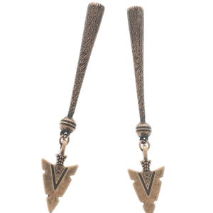 Puede incluir: Un par de pendientes de color bronce. Cada pendiente presenta una parte superior texturizada y alargada con una pequeña cuenta y un colgante en forma de punta de flecha en V. Los pendientes se muestran sobre un fondo blanco.