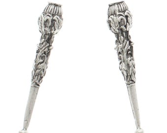 May include: A pair of silver-toned decorative finials with intricate floral designs. The finials are shaped like a pointed cone with a rounded top.