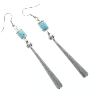 Puede incluir: Un par de pendientes de plata con una cuenta de turquesa azul claro en cada pendiente. Los pendientes tienen un colgante largo, delgado y plateado con una superficie texturizada.