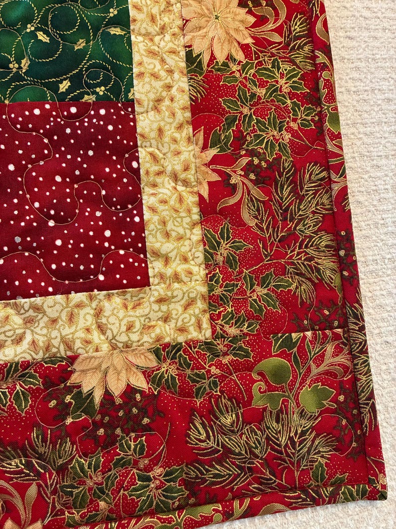 K&ouml;nnte beinhalten: Ein gesteppter Weihnachtstischl&auml;ufer mit Patchwork-Design. Der L&auml;ufer zeigt eine Kombination aus roten, gr&uuml;nen und goldenen Stoffen mit festlichen Mustern, darunter Weihnachtsstern, Stechpalme und Tupfen. Die Kanten sind mit einem passenden Rand sauber verarbeitet.