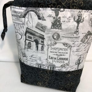 May include: A black and white drawstring bag with a Parisian theme. The bag features a print of the Eiffel Tower, a street lamp, and a vintage perfume bottle. The bag is lined with a black fabric with a gold swirl pattern.