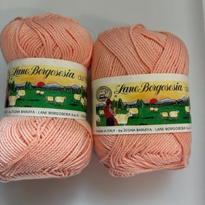 May include: Two peach-colored yarn skeins. Each skein has a label with the text "Lane Borgosesia" and a pastoral scene with sheep. The yarn is made in Italy by Zegna Baruffa.