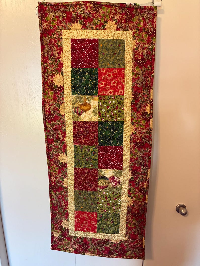 K&ouml;nnte beinhalten: Ein rechteckiger Weihnachtstischl&auml;ufer. Der L&auml;ufer hat ein Patchwork-Design mit roten, gr&uuml;nen und goldenen Quadraten. Der Rand ist tiefrot mit einem floralen Muster. Die mittleren Quadrate haben Weihnachtsschmuck und Sternmuster.