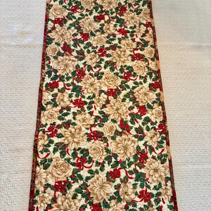 K&ouml;nnte beinhalten: Rechteckiger Weihnachtstischl&auml;ufer mit cremefarbenem Blumenmuster, roten Schleifen und gr&uuml;nen Stechpalmenbl&auml;ttern. Dunkelroter Rand. F&uuml;r festliche Tischdekoration.