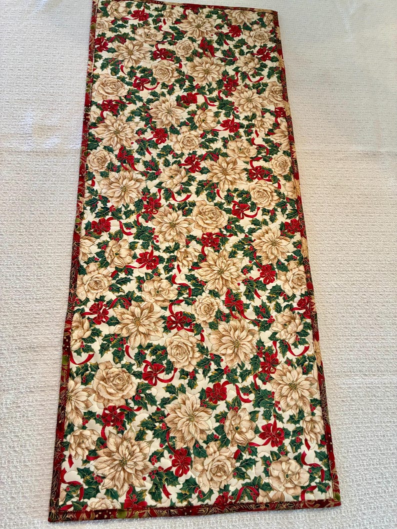 K&ouml;nnte beinhalten: Rechteckiger Weihnachtstischl&auml;ufer mit cremefarbenem Blumenmuster, roten Schleifen und gr&uuml;nen Stechpalmenbl&auml;ttern. Dunkelroter Rand. F&uuml;r festliche Tischdekoration.