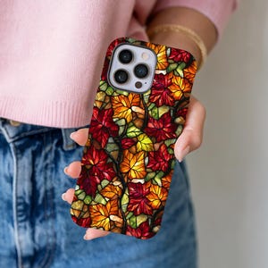 May include: A colorful phone case featuring a stained glass design of autumn leaves in shades of red, orange, and yellow. The case has a glossy finish and a protective design.