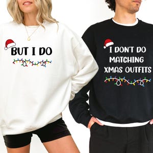 Könnte beinhalten: Zwei Weihnachtspullover, einer weiß und einer schwarz. Der weiße Pullover trägt den Text "BUT I DO", eine Weihnachtsmütze und Lichterketten. Der schwarze Pullover zeigt "I DON'T DO MATCHING XMAS OUTFITS", mit Weihnachtsmütze und Lichterketten.