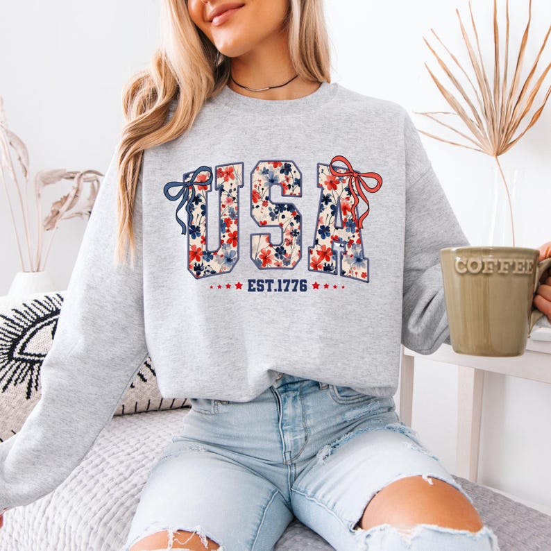 May include: A grey sweatshirt with a floral print of the word "USA" and the text "EST. 1776" below it.
