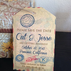 May include: A vintage-style save the date card with a brown background and blue text. The card features a stamp with the text "I Love You" and the date "10.12.13". The text "Please Save the Date" is printed in a large font, followed by the names "Cat & Jesse" in a smaller font. The date "October 12, 2013" and the location "Pomona, California" are printed below the names. The card also features a stamp with the text "Air Mail" and a plane.