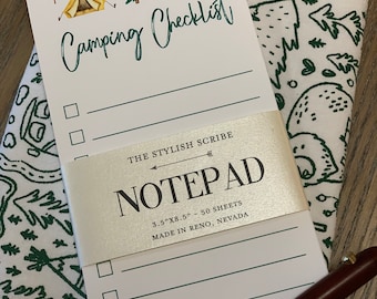 May include: A white notepad with a green and brown camping checklist design. The notepad has a silver label that reads "The Stylish Scribe Notepad 3.5"x8.5" - 50 Sheets Made in Reno, Nevada".